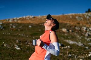 A female hiker enjoys a warm cup of tea while resting after a challenging mountain climb.A woman hiker takes a peaceful break, sipping tea and enjoying the view after a strenuous mountain climb photo