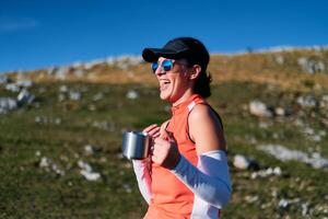 A female hiker enjoys a warm cup of tea while resting after a challenging mountain climb.A woman hiker takes a peaceful break, sipping tea and enjoying the view after a strenuous mountain climb photo