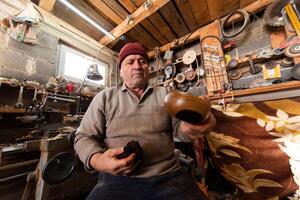 A senior man sitting in the workshop and smearsing wooden utensils with linseed oil photo