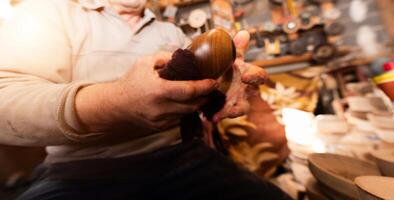 A senior man sitting in the workshop and smearsing wooden utensils with linseed oil photo