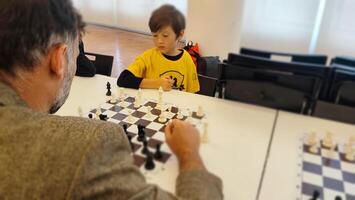 chessplayer. Clever junior school age boy playing chess with dad planning gambit moving black piece on chessboard. Preteen son engaged in brain developing activity enjoy board game with father photo