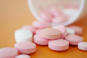 Pink and white tablets scattered on a surface from a tipped container photo