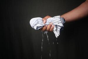 Hand squeezing a wet cloth with water dripping in low light photo