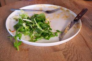 Leftover salad on a plate with utensils after meal photo
