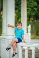 A young boy sitting on a pillar in a park photo