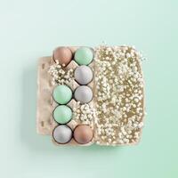 Pastel Easter Eggs with white Flowers in Carton box on mint Background, top view chicken egg painted turquoise beige colors. Easter celebration concept. Festive food, minimal still life holiday photo