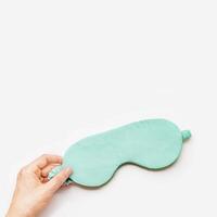 Sleeping mask for healthy quality sleep in woman hand on white light background, copy space. Mint colored accessory for best sleeps. Fashion silk eye mask for travel, comfort rest, minimal view photo