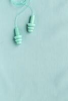 Reusable silicone earplugs mint color on color textile background, copy space. Against noise and water Ear plug on string, for swim, sleep, protect hear, aesthetic top view, minimal style photo