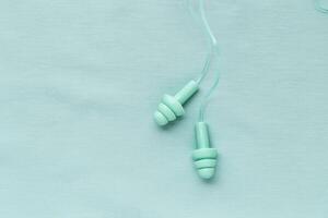 Reusable silicone mint earplugs on colored textile background, copy space. Against noise and water Ear plug on string, for swim, sleep, protect hear, aesthetic top view, minimal style photo