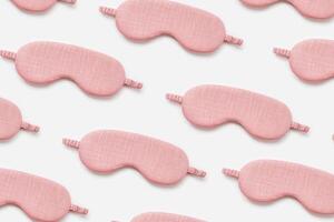 Minimal style pattern from pink sleep masks on white background. Trend Colored fashion eye masks for best sleeper, for travel, comfort rest. Night time and sleep concept, flat lay composition photo