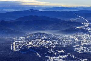 Winter nature panorama with Sheregesh ski resort in Altai, Russia, picturesque view, aerial tonal perspective, abstract background with range mountains white and blue sky, hills covered trees photo