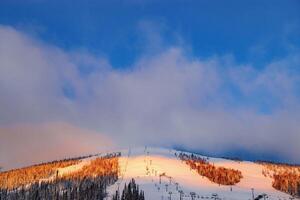 Picturesque sunrise and winter mount covered snow and forest, pink clouds on sky, white snow slopes and ski traces, view on mountain Green mount Zelenaya, Sheregesh ski resort in Russia photo