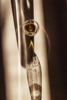 glass of cognac sparkling at sunlight, beige background with dark shadow and reflection, sun flare light effect on table. Strong alcohol drink with star filter, top view, desaturated colors photo