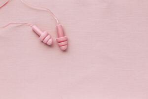 Reusable silicone earplugs pink color on colored textile background, copy space. Against noise and water Ear plug on string, for swim, sleep, protect hear, aesthetic top view, minimal style photo