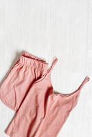 Pink pajamas on white wooden background with copyspace. Summer night suit for sleeping, folded clothes singlet and shorts top view photo. Woman sleepwear minimal flat lay style, comfort sleep photo