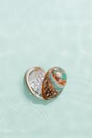 Minimal aesthetic scene, heart of iridescent seashells in waves seawater at sunlight, natural beauty marine life, connection with nature, tranquility, meditation. Shell as symbol of love photo