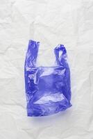 Plastic free concept, top view blue crumpled plastic bag crumpled on white wrinkled paper background. Disposable polythene packet for food. Eco trend minimal style photo, vertical photo, above photo