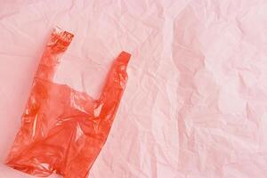 Plastic free concept, top view crumpled plastic bag crumpled on pink wrinkled paper background, copy space. Disposable polythene packet for food. Eco trend minimal style photo, red monochromatic photo