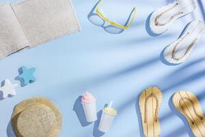 Summer flat lay frame with sunglasses, sun hat, beach flip flops, ice cream, top view cute toys on blue background, copy space. Summer rest vibes, beach relaxation, palm leaf shadow, aesthetic photo