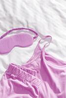 Top view fuchsia colored pajama and eye sleep mask on white crumpled bedclothes. Cozy pyjamas for comfort rest at night. Flat lay singlet, shorts, sleeping mask pastel pink color, sleep well photo