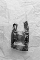 Plastic free concept, black and white, top view crumpled plastic bag crumpled on wrinkled paper background. Disposable polythene packet for food. Eco trend minimal style photo, monochrome photo