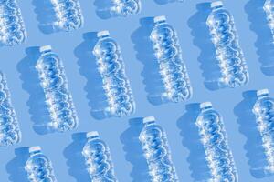 Minimal Pattern Plastic bottles water at sunlight, shadow on blue, aesthetic top view. Distilled drinking water. Pollution, environmental protection. Eco trend to reduce disposable plastics photo