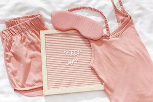 Sleep day holiday concept, Pink female pajama, sleep eye mask on white cloth bed sheet. Felt board with text, Top view pretty pyjamas for health sleeping. Romance mood, delicate image photo