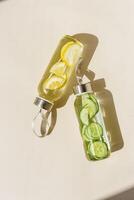 Glass bottle with lemon and cucumber water drink detox at sunlight on beige table background, copy space, sun glare. Natural Infused water Healthy drink. Aesthetic still life, refreshing drink photo