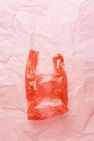 Plastic free concept, top view plastic bag crumpled on pink wrinkled paper background, copy space. Disposable polythene packet for food. Eco trend minimal style photo, red monochrome photo