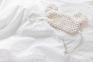 Sleep mask ofsoft nice fur on bed with white pillow and blankets bedclothes. Cozy life style home image. Fluffy eye cover mask for best sleep. Concept of home comfort, top view, flat lay photo