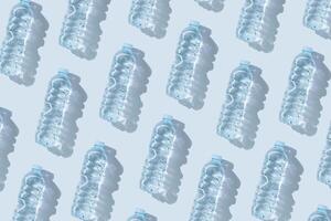 Pattern small plastic bottles with clean drinking water at sunlight, shadow on blue background. Full closed bottle water half litre. Pollution, plastic garbage, non-biodegradable packaging waste photo