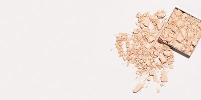 Crushed light beige foundation powder cosmetics swatch. Makeup powder texture on beige background, wide banner with empty space. Nude broken eye shadow. Skin tone face cosmetic product sample photo