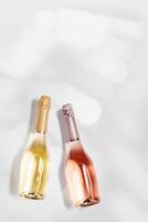 Top view sparkling wine, bottles of rose and white champagne wit sunlight flare on grey colored background, copy space for text. Festive alcohol drink, wedding party drink concept, minimal card photo