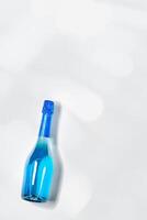 Minimal Top view sparkling wine with sun shadow and glare, romance beverage, blue bottle of champagne on light white gray background, copyspace. Festive Summer alcohol drink concept, aesthetic photo
