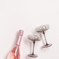 Rose Champagne or sparkling wine bottle, wine glasses grey glass. Romance festive drink concept, glare from sunlight. Modern wine colored glasses. Minimal creative aesthetic flat lay, copy space photo