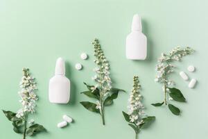 Seasonal spring allergies, spring branches tree with flowers and mock up nasal spray bottle, pills on green background, Concept of allergy to flowering. Antihistamine spray for nasal congestion. photo