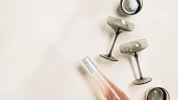 Rose wine bottle , wine glasses from tinted grey glass on beige background, copy space. Minimal style summer drink concept. Trendy vintage colored glass. Creative top view, light effect, glare photo