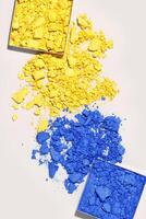Yellow and blue colored broken eye shadow cosmetics swatches, aesthetic beauty texture flat lay, beige background. Crumbling eye shadows make up powder sample, woman cosmetics and beauty product photo