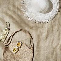 Beach still life at summer sun, fashion jute beach bag, detox lemon water, sun hat, sunglasses on beach towel, summer relax concept, image of modern stylish relaxing on beach, top view, space photo