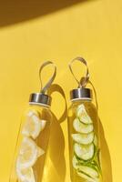 Cleansing and refreshing water drink detox with slices of lemon and cucumber, shadow at sunlight on yellow. Wellness, diet, eating healthy concept. Stylish glass reusable water bottle top view photo