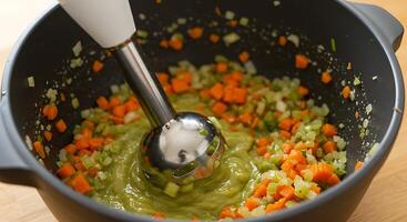 Creamy Vegetable Soup Preparation with Immersion Blender in Dark Bowl photo