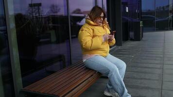Digital AI chatbot, Happy Caucasian woman in yellow jacket and sunglasses using mobile smartphone with AI chatbot for online information in city town, conversation assistant. video