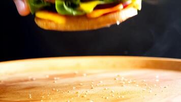 A close-up of a hand reaching for a delicious cheeseburger with lettuce, tomato, onion, and melted cheese on a sesame seed bun. . High quality 4k footage video