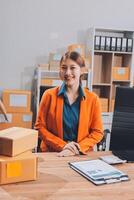 A woman in an orange jacket sitting at a desk with boxes photo