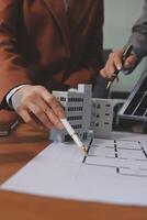A man is holding a pen and pointing at a model of a building photo