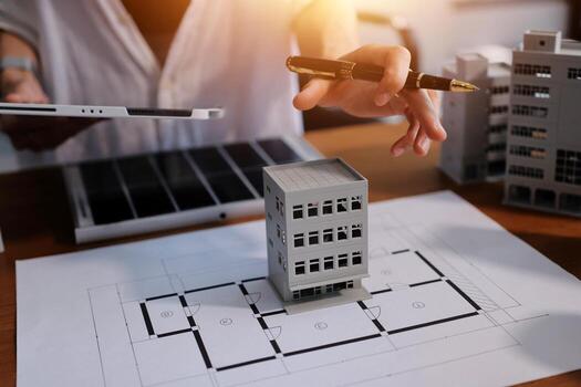 A person is holding a pen and pointing at a model of a building photo