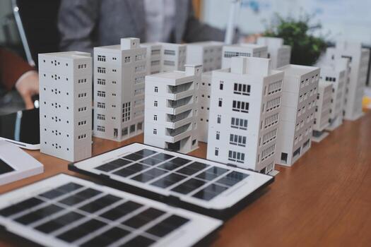 A table with a solar panel, a laptop and a paper model of a building photo