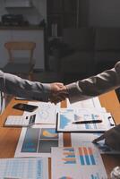 Business people shaking hands over a table with papers and graphs photo