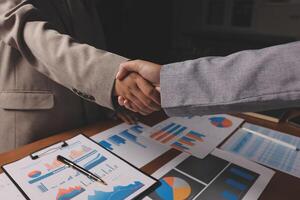 Business people shaking hands over a table with graphs and papers photo