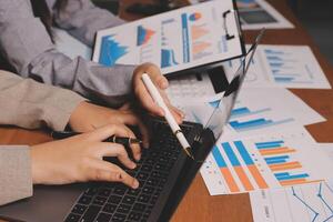 Business people working on laptops with graphs and papers photo